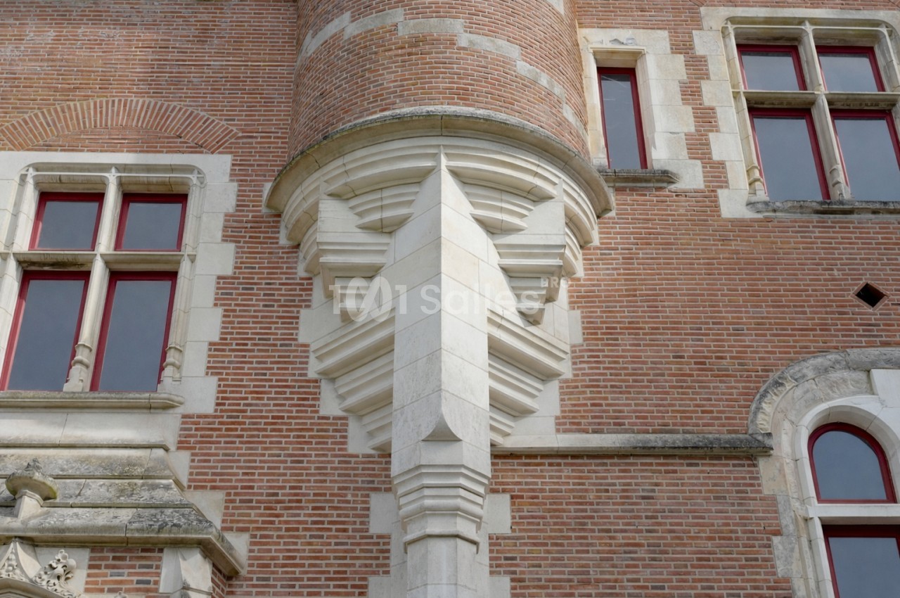 Détail d'une façade en briques rouges avec des fenêtres à encadrement blanc et un élément architectural en pierre sculptée.
