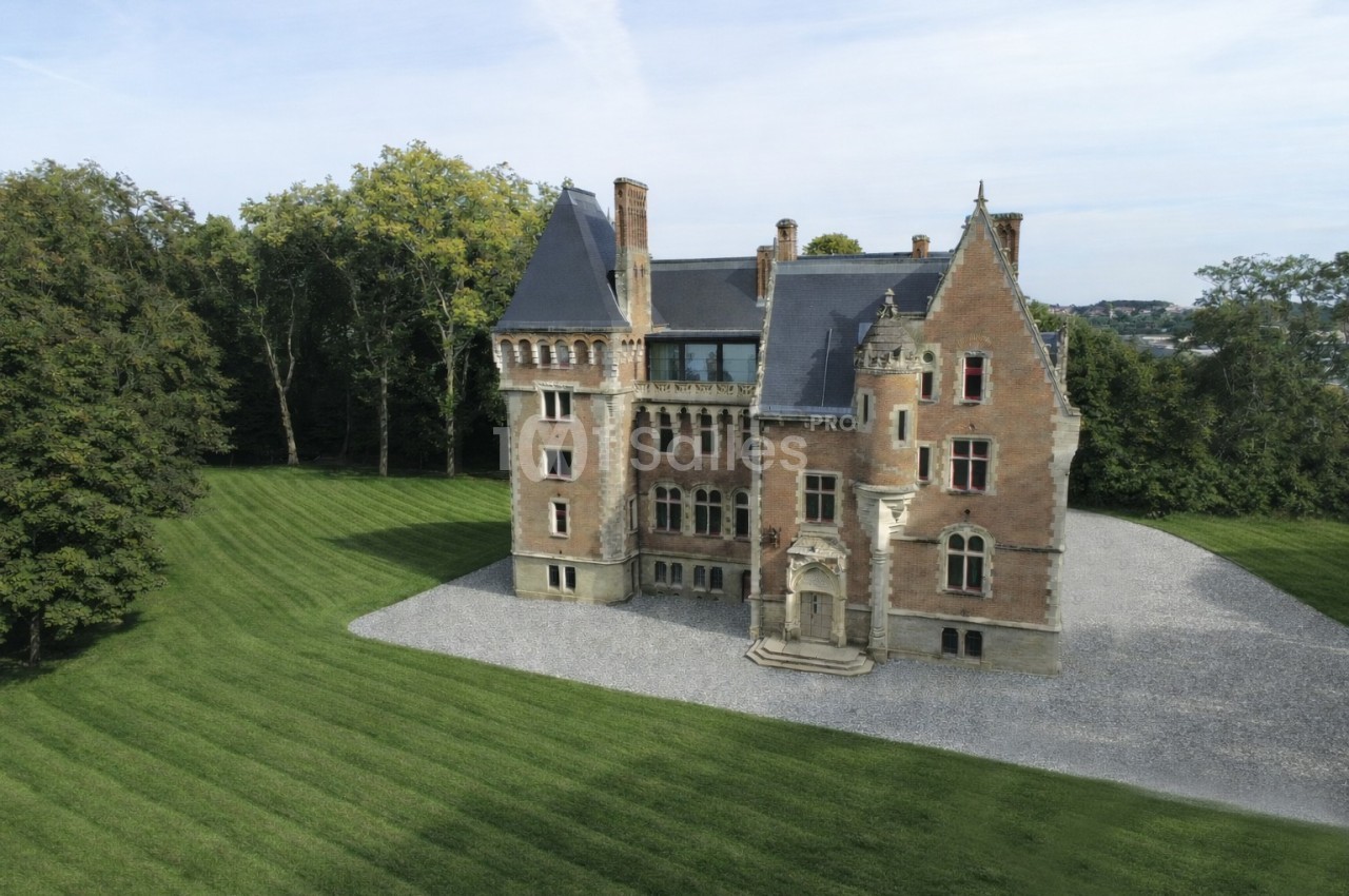 Vue aérienne d'un château en briques rouges entouré de pelouses bien entretenues et d'arbres.