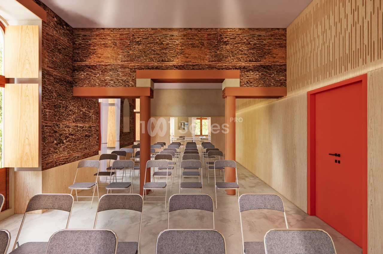 Salle lumineuse avec des rangées de chaises grises, murs en bois texturé et porte rouge sur le côté droit.