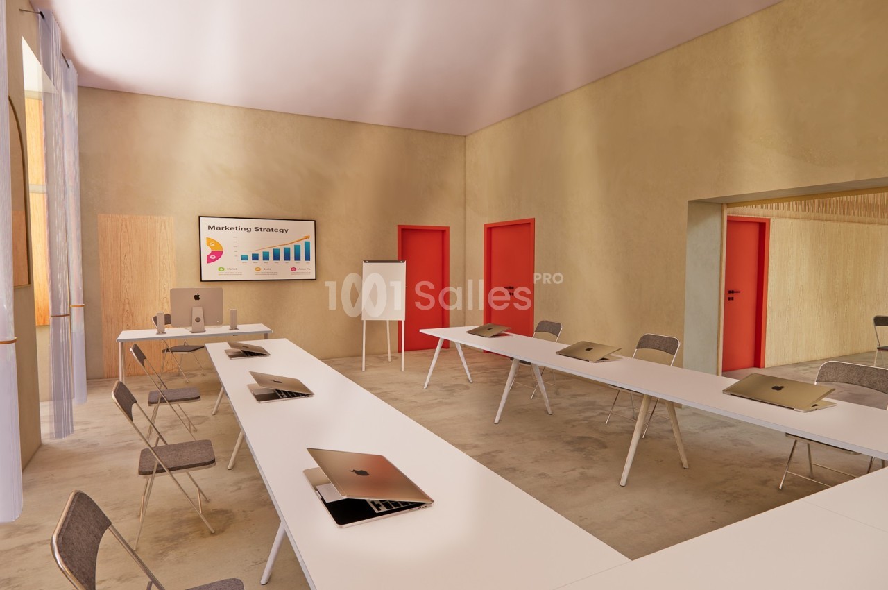 Salle de réunion lumineuse avec tables en U, chaises, ordinateurs portables et écran affichant une présentation.