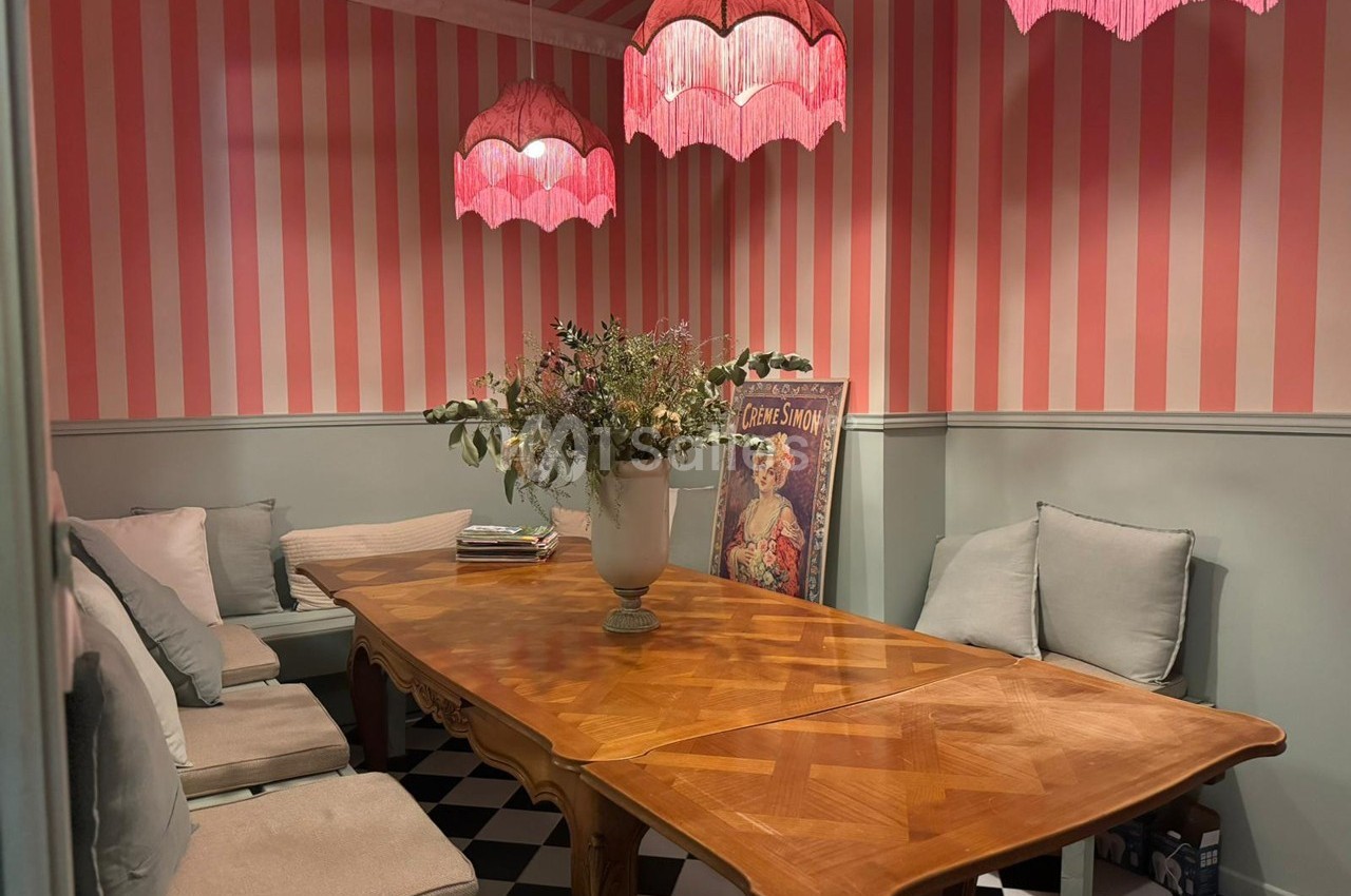 Salle à manger avec table en bois, banquettes et coussins, murs à rayures roses et blanches, luminaires roses suspendus.