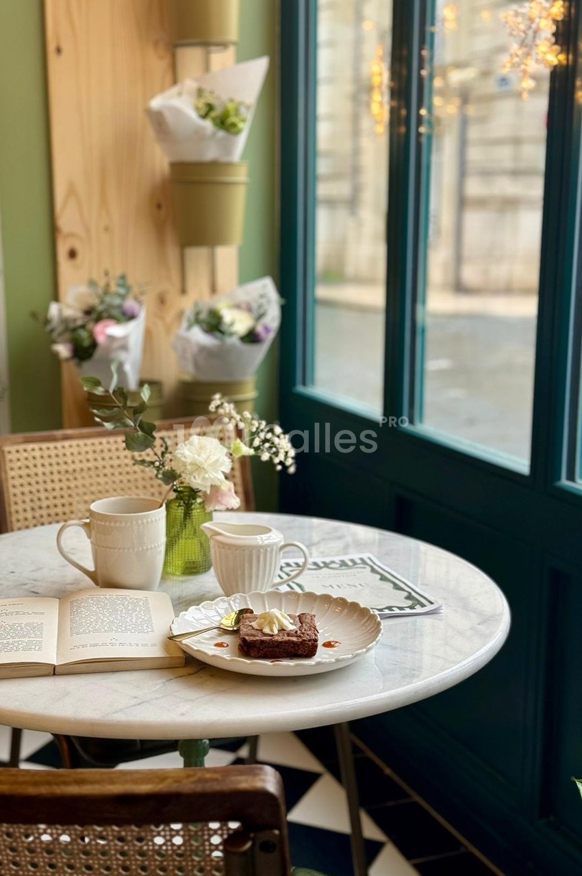 Table en marbre avec deux tasses, un livre ouvert et une assiette de gâteau, près d'une fenêtre lumineuse et décorée de…