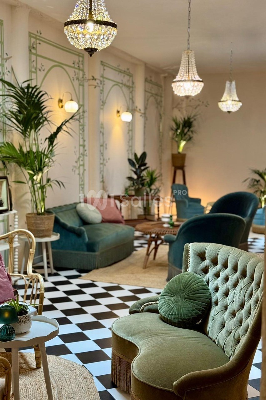 Salon élégant avec fauteuils verts, plantes, lustres en cristal et sol en damier noir et blanc.
