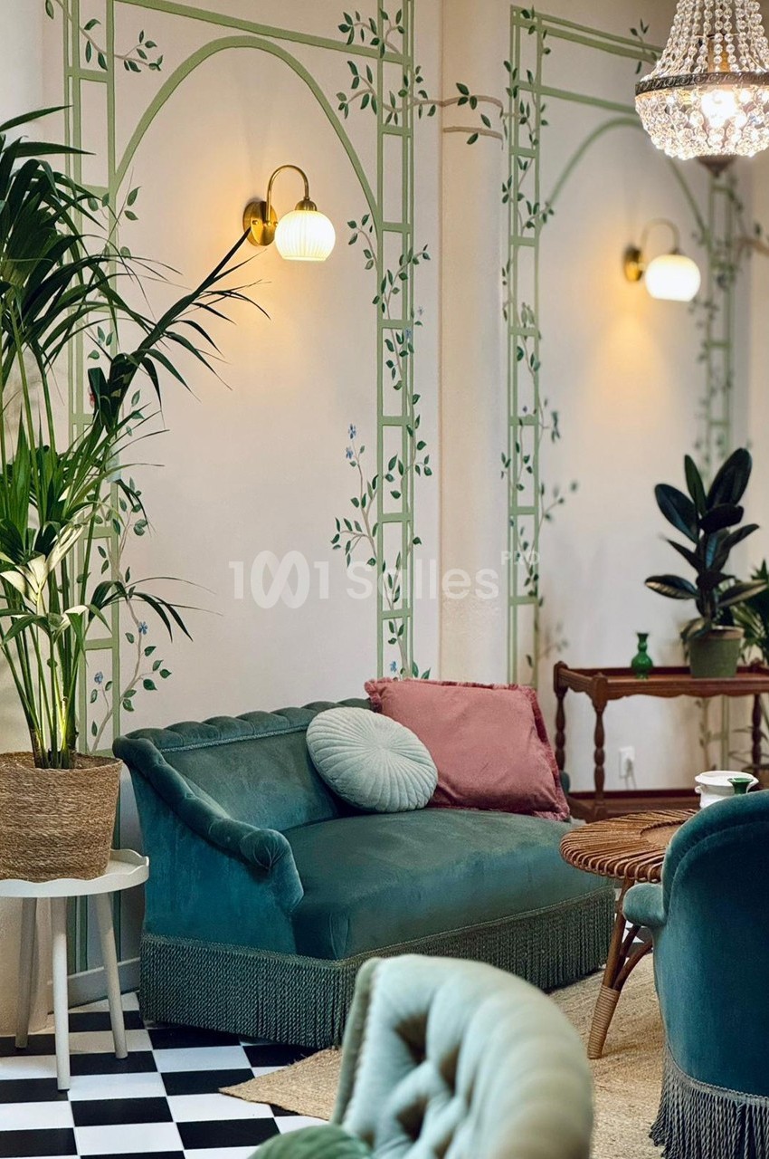 Salon élégant avec canapé vert, coussins, plantes en pot, table en bois et murs décorés de motifs végétaux.
