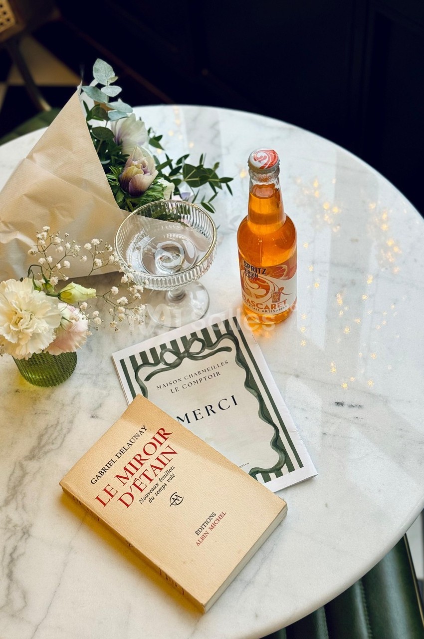 Livre, fleurs blanches, bouteille de soda et carte posés sur une table en marbre dans un cadre élégant.
