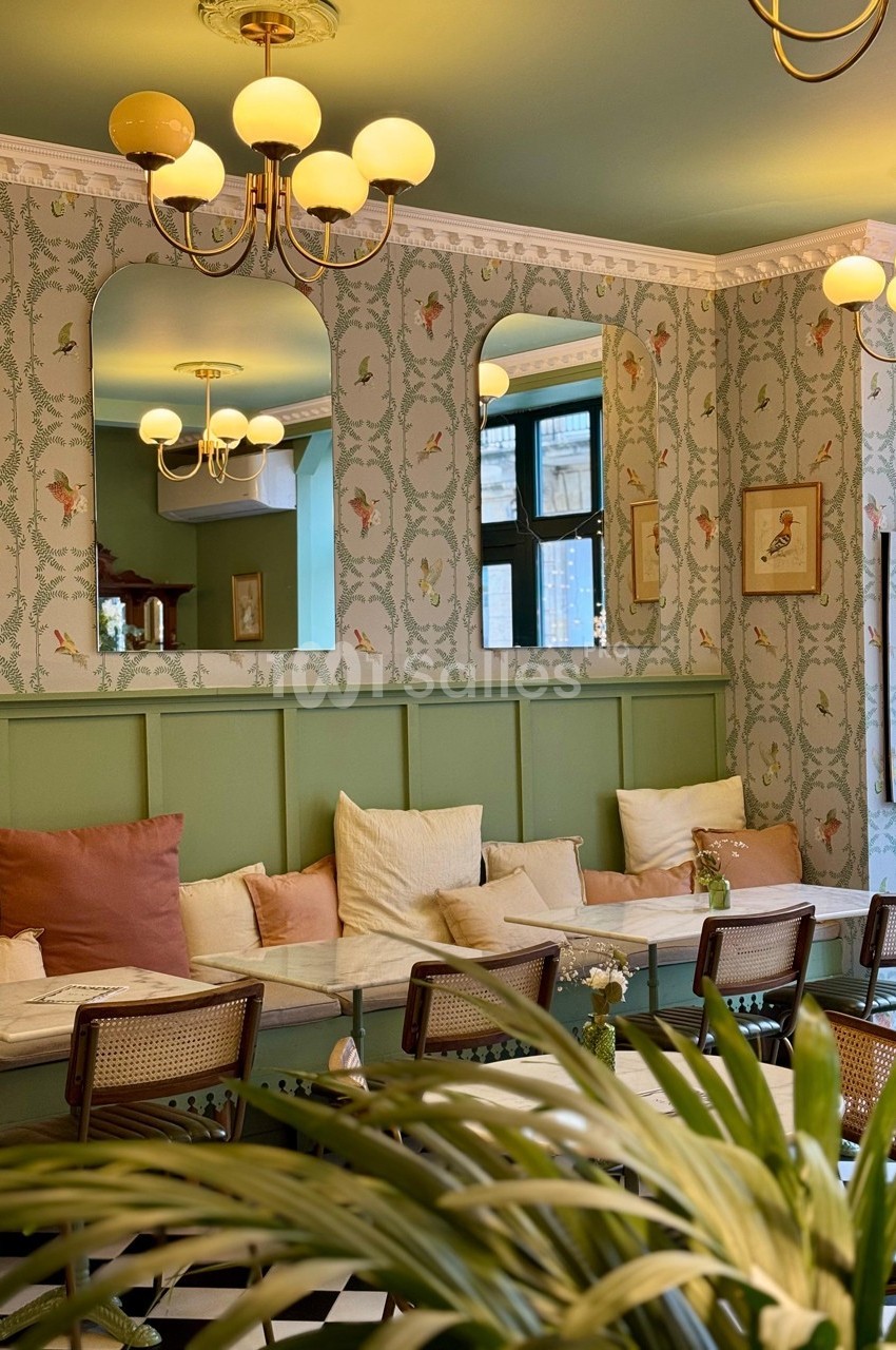 Salle de restaurant lumineuse avec banquette, coussins colorés, miroirs et décoration murale à motifs floraux.