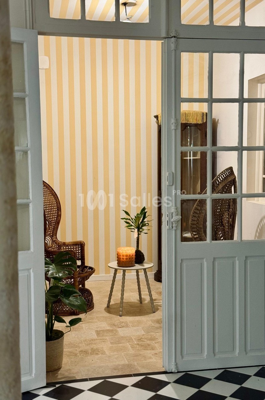Vue d'un salon lumineux avec fauteuils en rotin, table basse décorée d'une plante et bougie, sol en pierre beige.