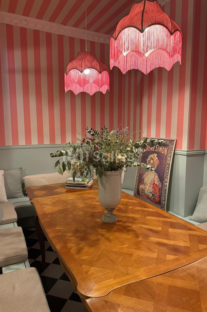 Salle à manger avec table en bois, banquettes rembourrées, lampes à franges roses et vase de fleurs au centre.