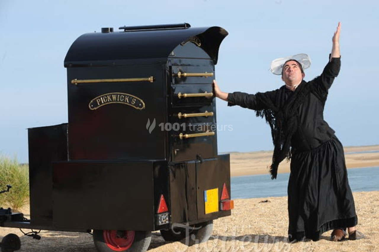 Un homme en tenue traditionnelle pose de manière théâtrale près d'un four mobile sur une plage.