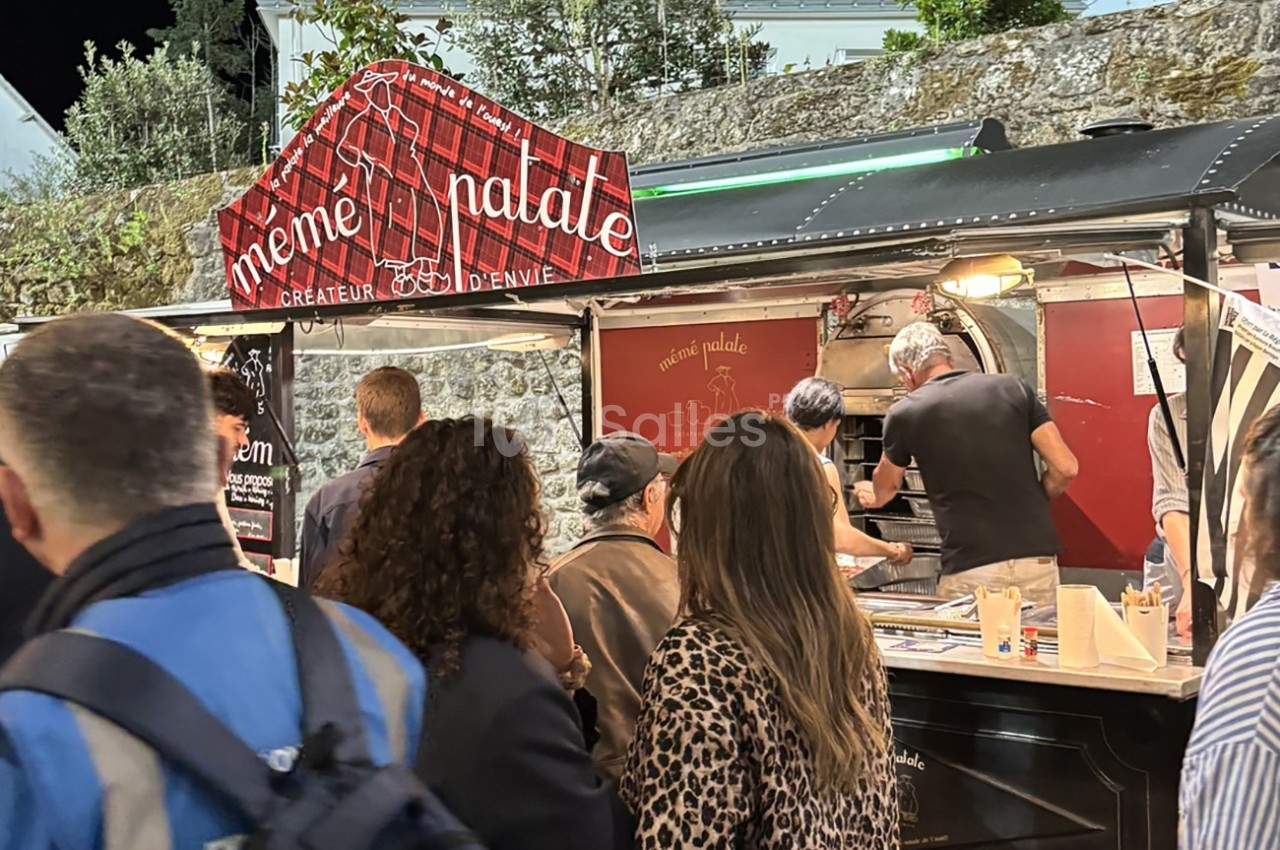 File d'attente devant un food truck avec des clients commandant et un cuisinier préparant des plats.