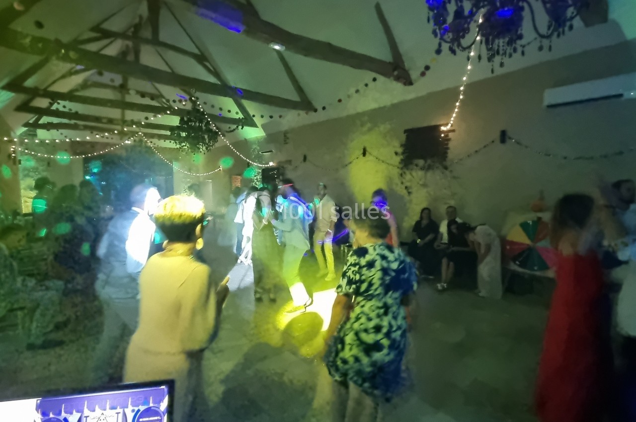 Des personnes dansent dans une salle décorée avec des guirlandes lumineuses et éclairée par des jeux de lumière colorés.