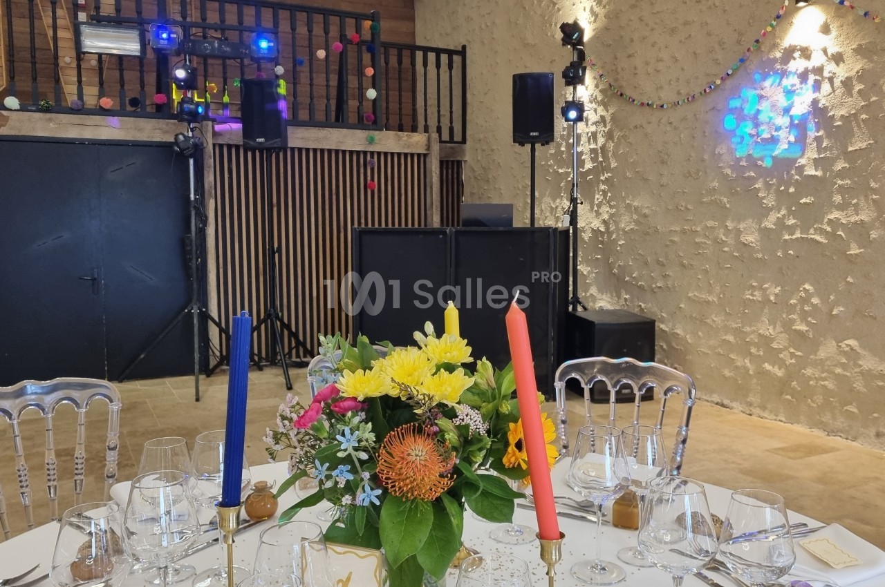 Table décorée avec des fleurs colorées et bougies, dans une salle avec piste de danse et éclairages festifs.
