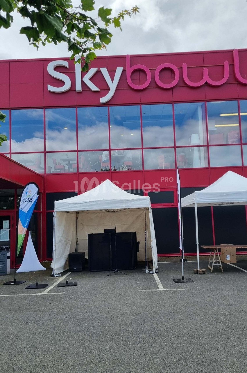 Façade d'un bâtiment rouge avec l'enseigne ’Skybowl’, devant laquelle sont installées des tentes blanches.