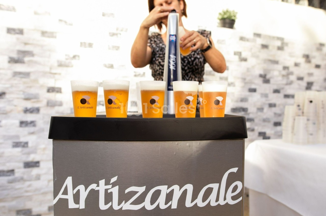 Une personne sert des bières artisanales dans des verres alignés sur un comptoir lors d'un événement en extérieur.