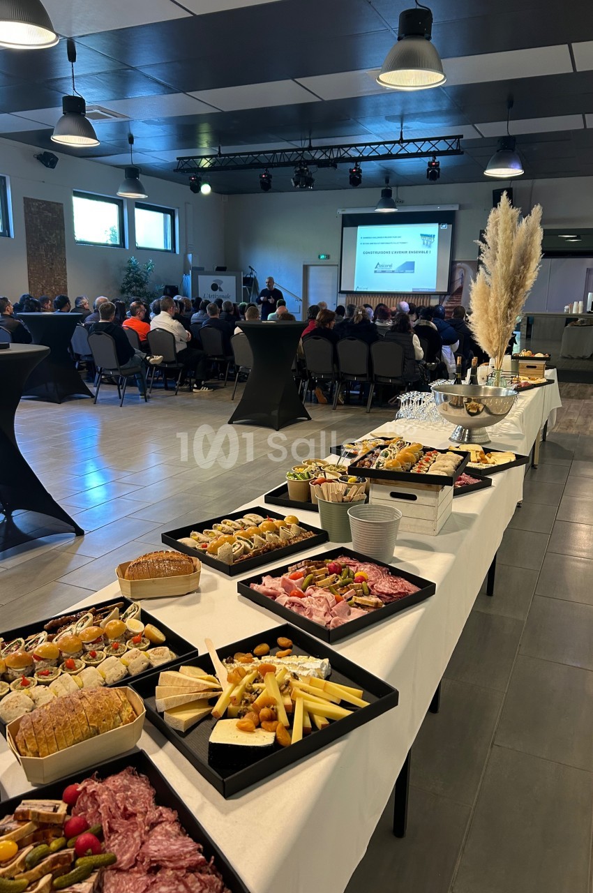 Buffet de charcuterie et amuse-bouches en premier plan, avec une présentation devant un public en arrière-plan.