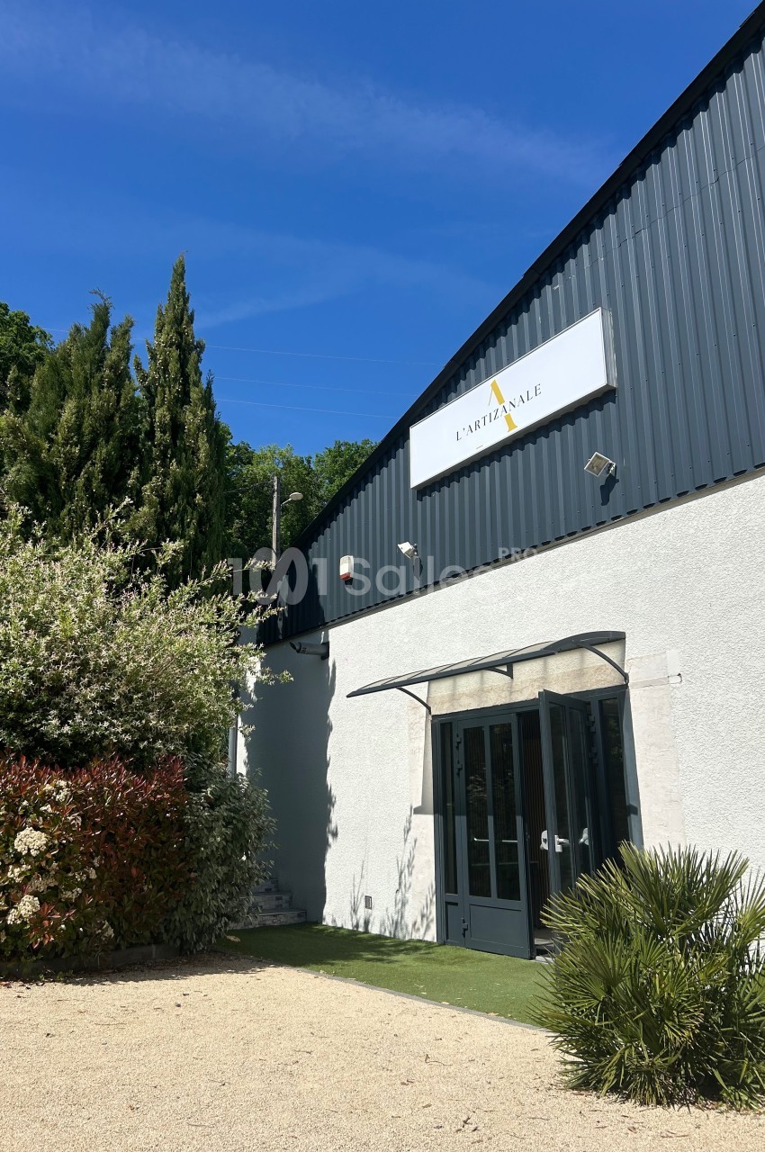 Façade d'un bâtiment avec un panneau ’L'Artisanale’, entouré de végétation sous un ciel bleu.