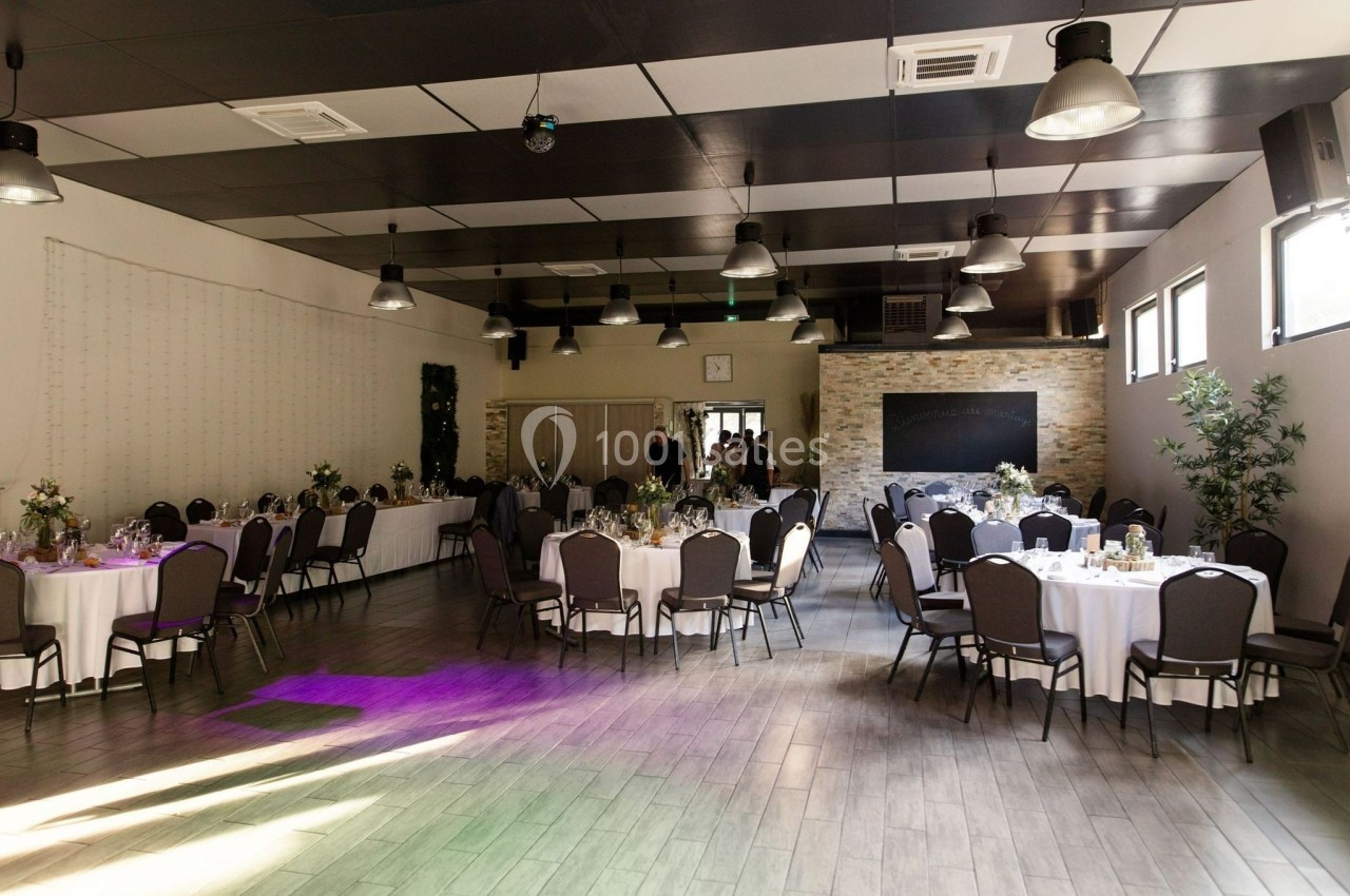 Salle de réception lumineuse avec tables rondes décorées, chaises noires et éclairage suspendu moderne.