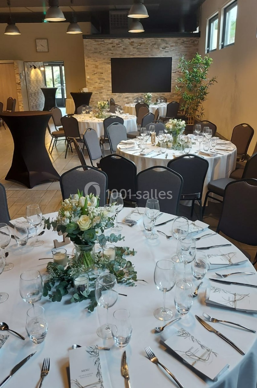 Salle de réception décorée avec des tables rondes dressées, ornées de bouquets de fleurs et de menus élégants.