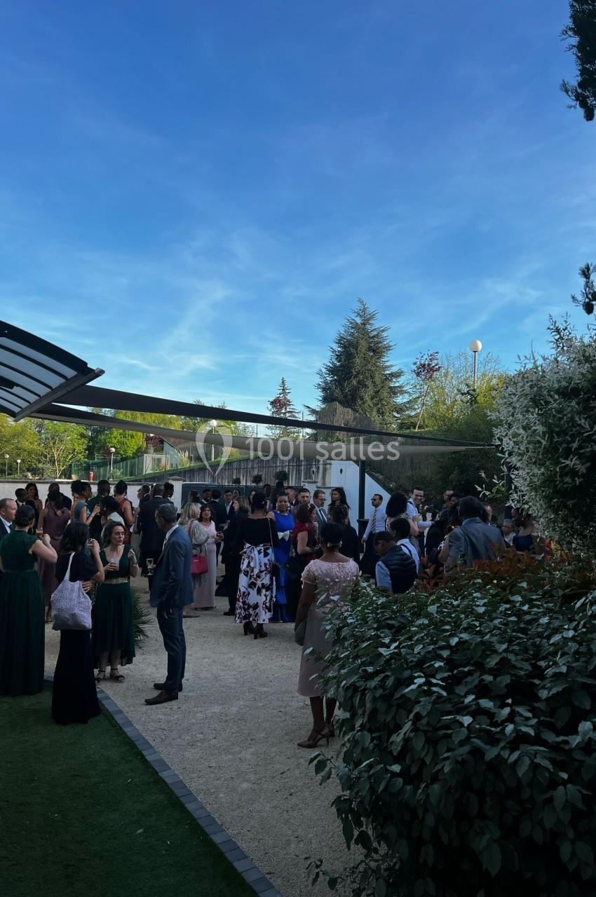 Groupe de personnes rassemblées en extérieur dans un jardin sous un ciel bleu, lors d'un événement ou d'une réception.