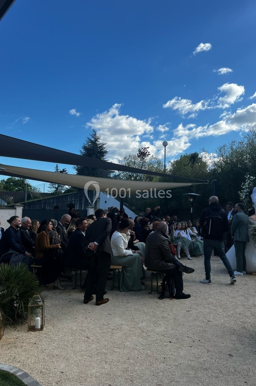 Un groupe de personnes assises en extérieur lors d'une cérémonie sous un ciel partiellement nuageux.