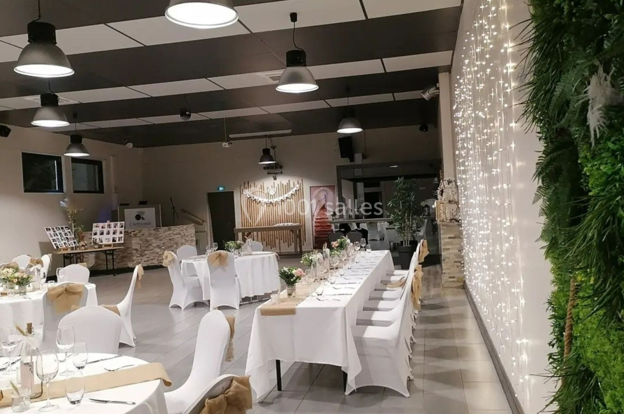 Salle de réception décorée avec des tables dressées, des guirlandes lumineuses et un mur végétal.