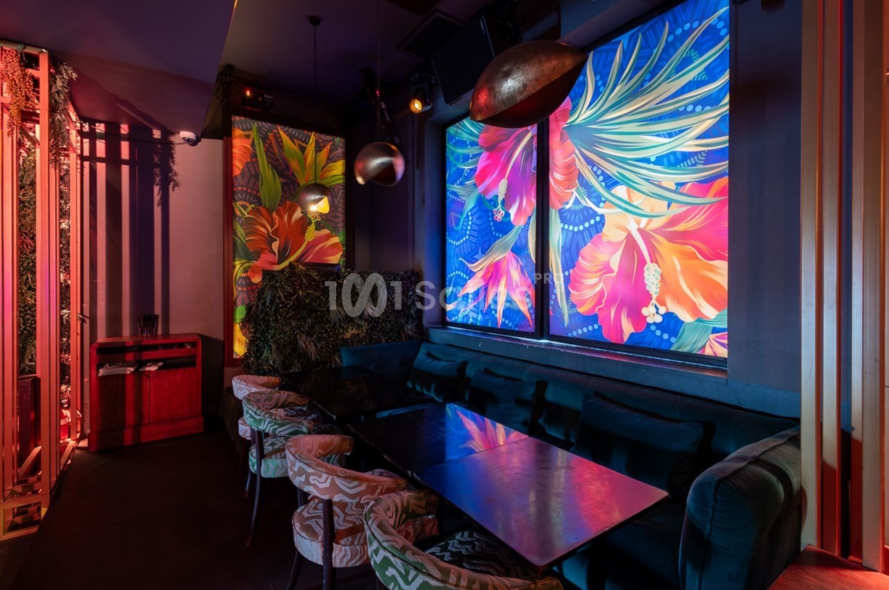 Salle de restaurant avec banquettes, table en verre et décorations murales colorées représentant des fleurs tropicales.
