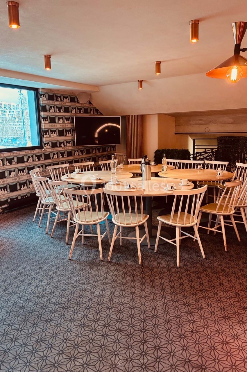 Salle de réunion lumineuse avec une grande table ronde entourée de chaises en bois, décorée de tons chaleureux.