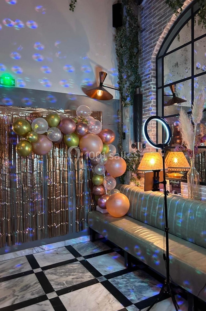 Décoration festive avec arche de ballons colorés, rideau scintillant et éclairage dans un espace intérieur élégant.