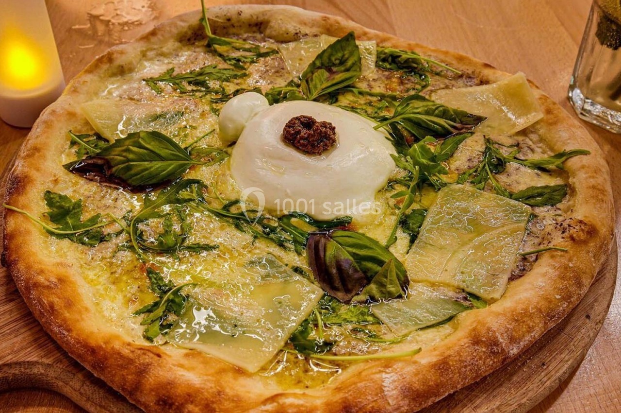 Pizza garnie de burrata, roquette, basilic, copeaux de fromage et tomate séchée, servie sur une planche en bois.