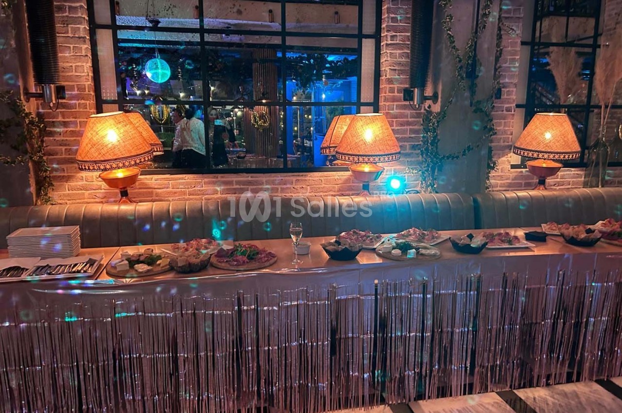 Table de buffet décorée avec des plats variés, éclairée par des lampes et entourée d'une ambiance lumineuse tamisée.