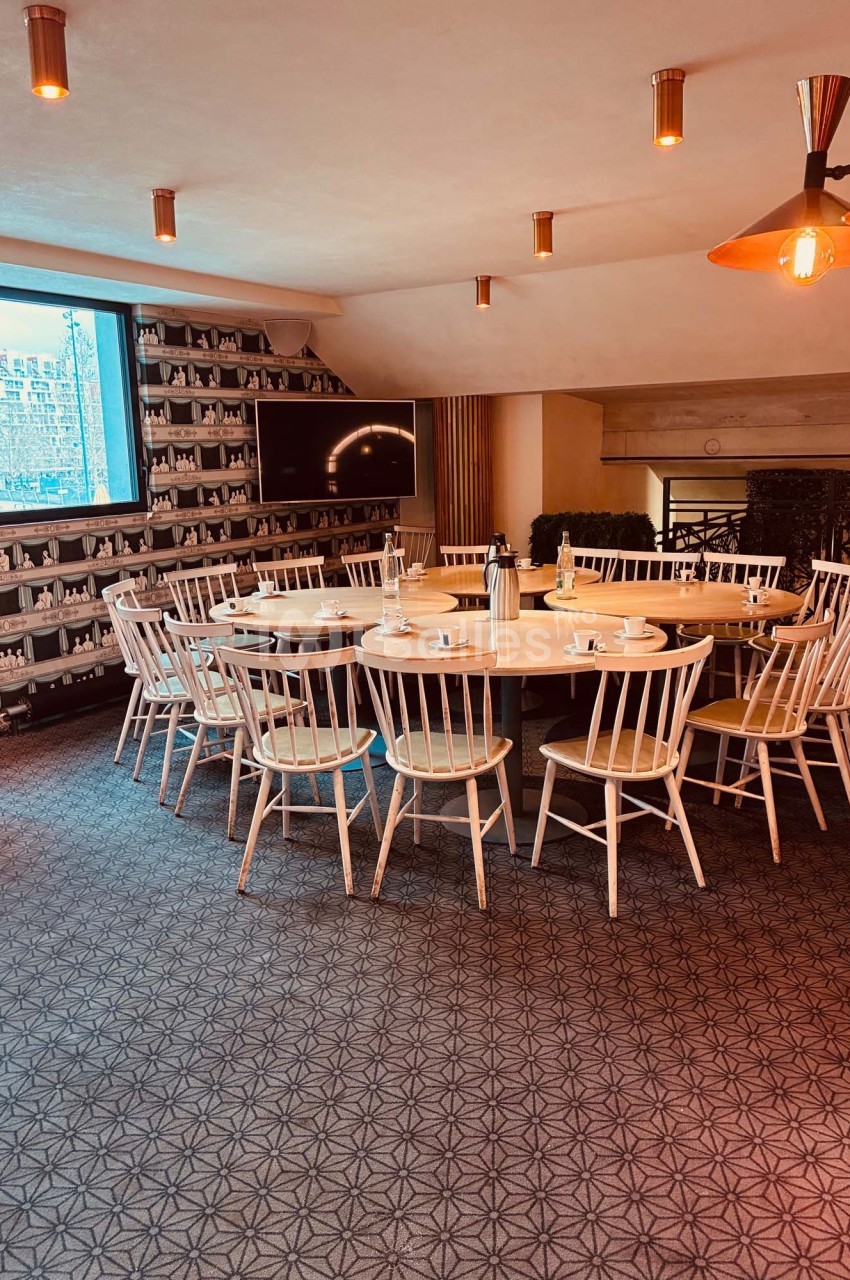 Salle de réunion lumineuse avec une grande table ronde entourée de chaises en bois, décorée de tons chaleureux.