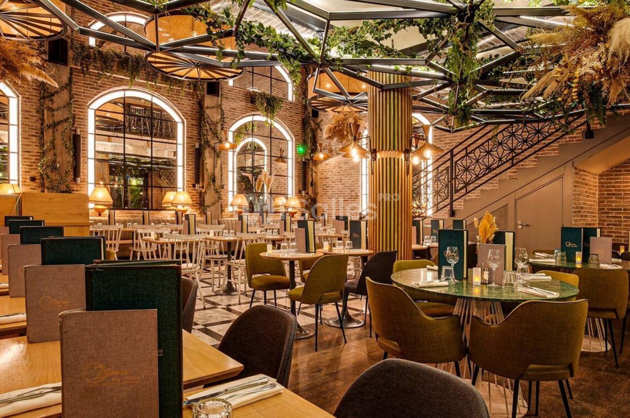 Salle de restaurant élégante avec tables dressées, décoration végétale et éclairage chaleureux.