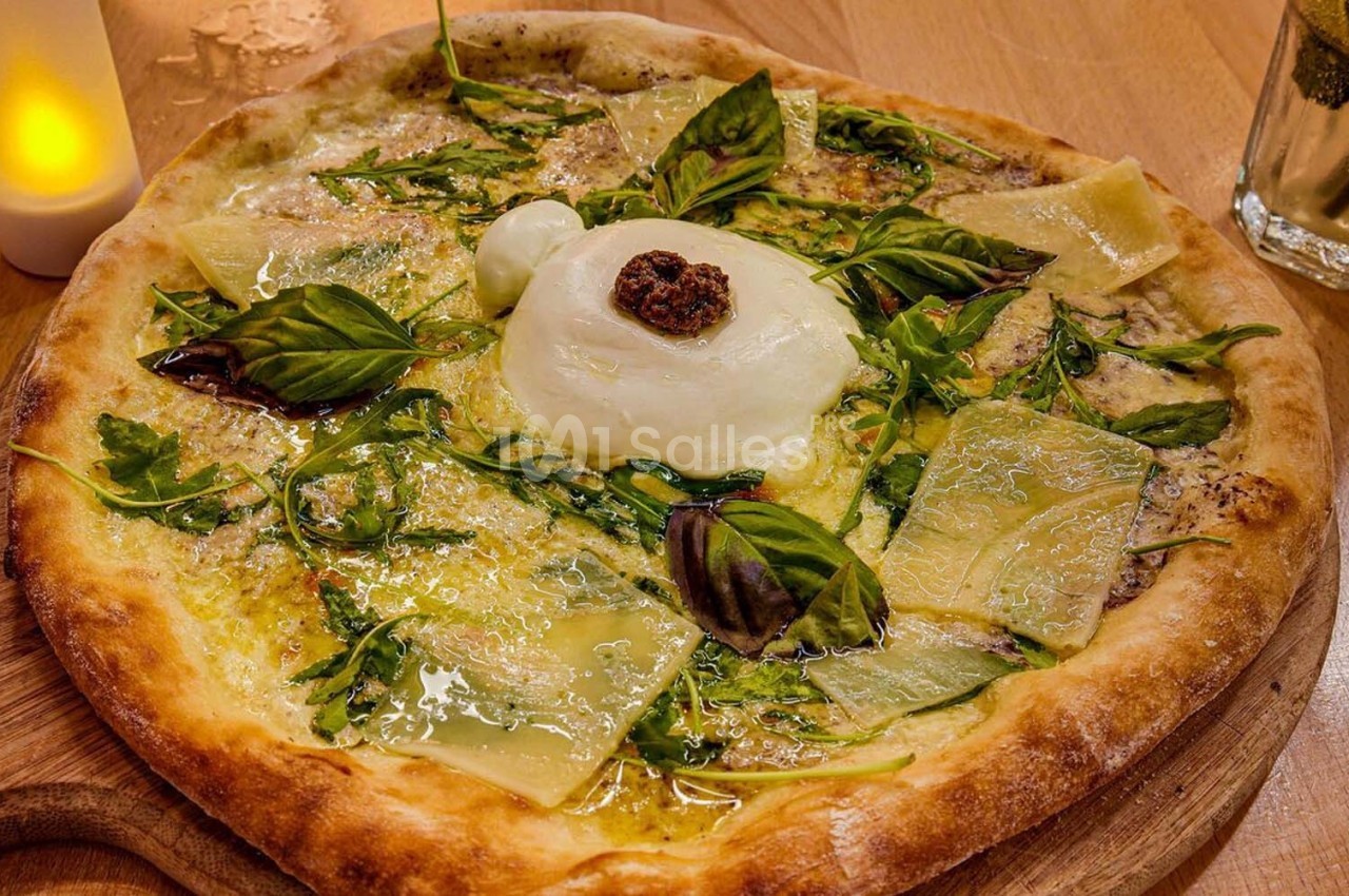 Pizza garnie de burrata, roquette, basilic, copeaux de fromage et tomate séchée, servie sur une planche en bois.