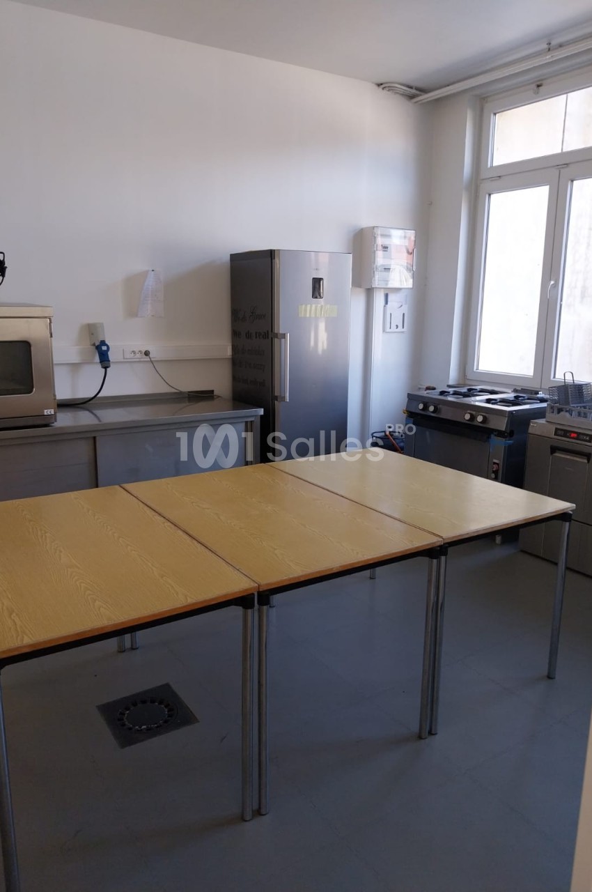 Cuisine équipée avec plan de travail, réfrigérateur, four, plaques de cuisson et lave-vaisselle, éclairée par une fenêtre.