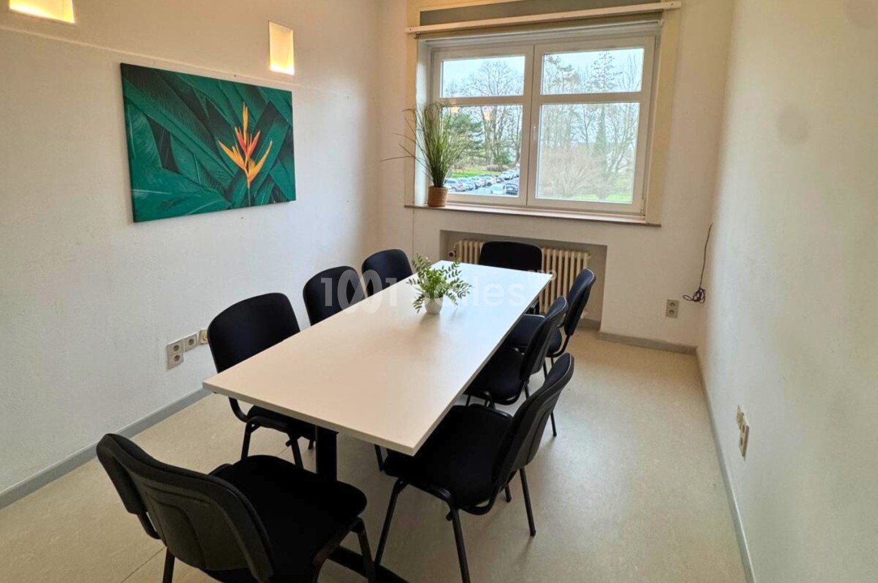 Salle de réunion lumineuse avec une table blanche, six chaises noires, une plante et une fenêtre donnant sur l'extérieur.