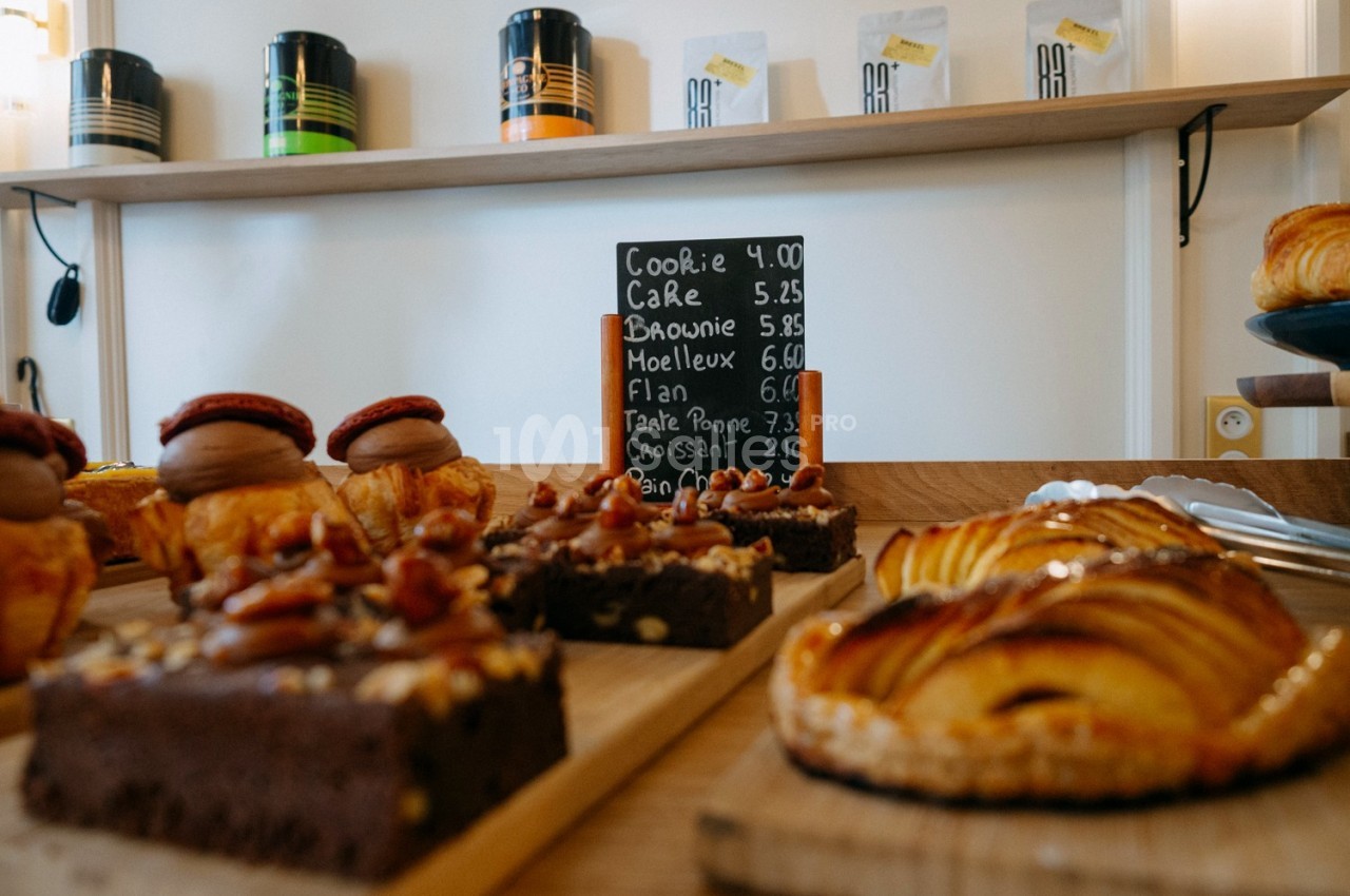 Pâtisseries variées sur un comptoir en bois avec une ardoise indiquant les prix en arrière-plan.