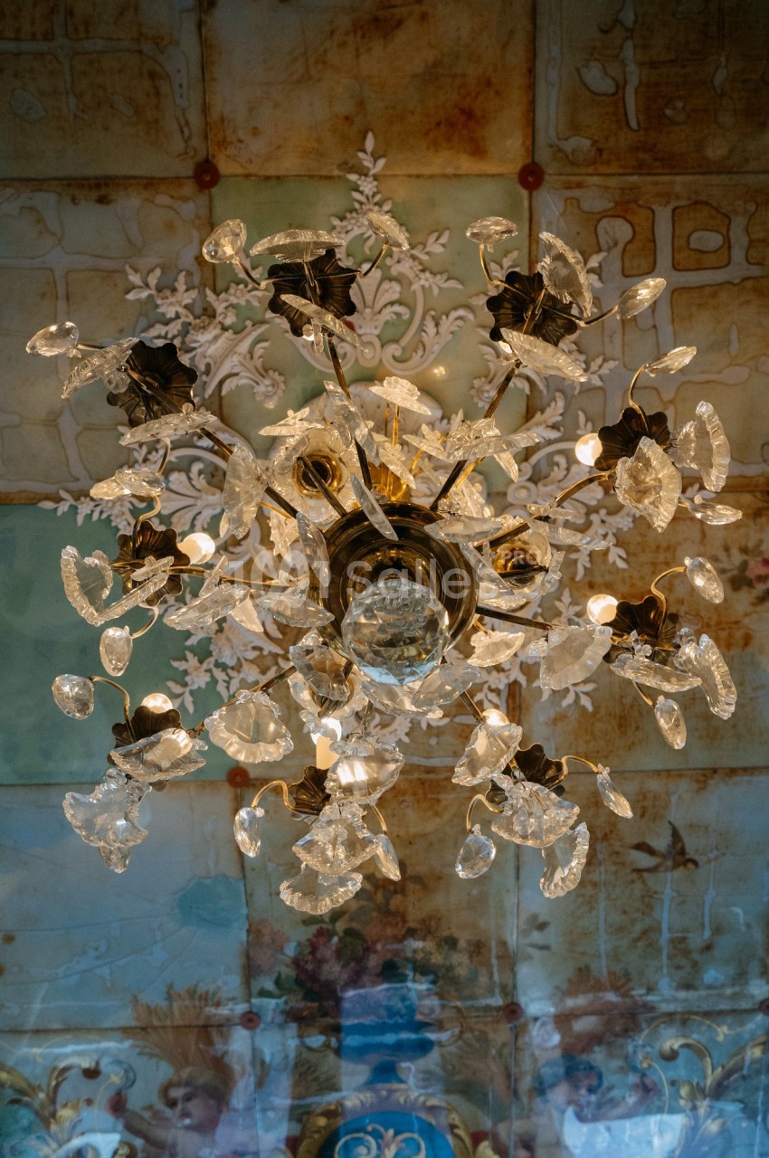 Lustre en cristal suspendu, éclairé, avec un plafond décoratif peint en arrière-plan.