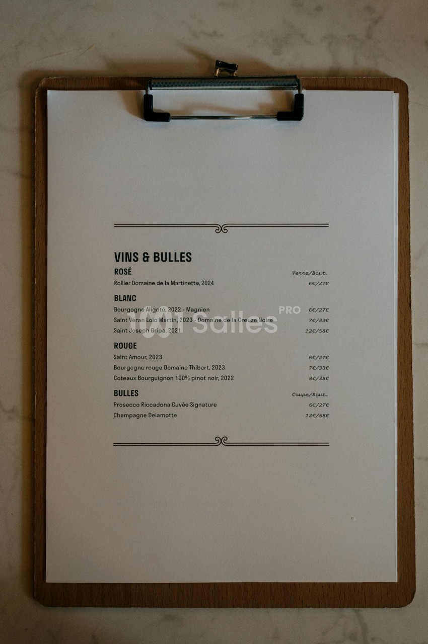 Carte des vins et bulles imprimée sur une feuille blanche fixée à une planchette en bois, posée sur une surface en marbre.