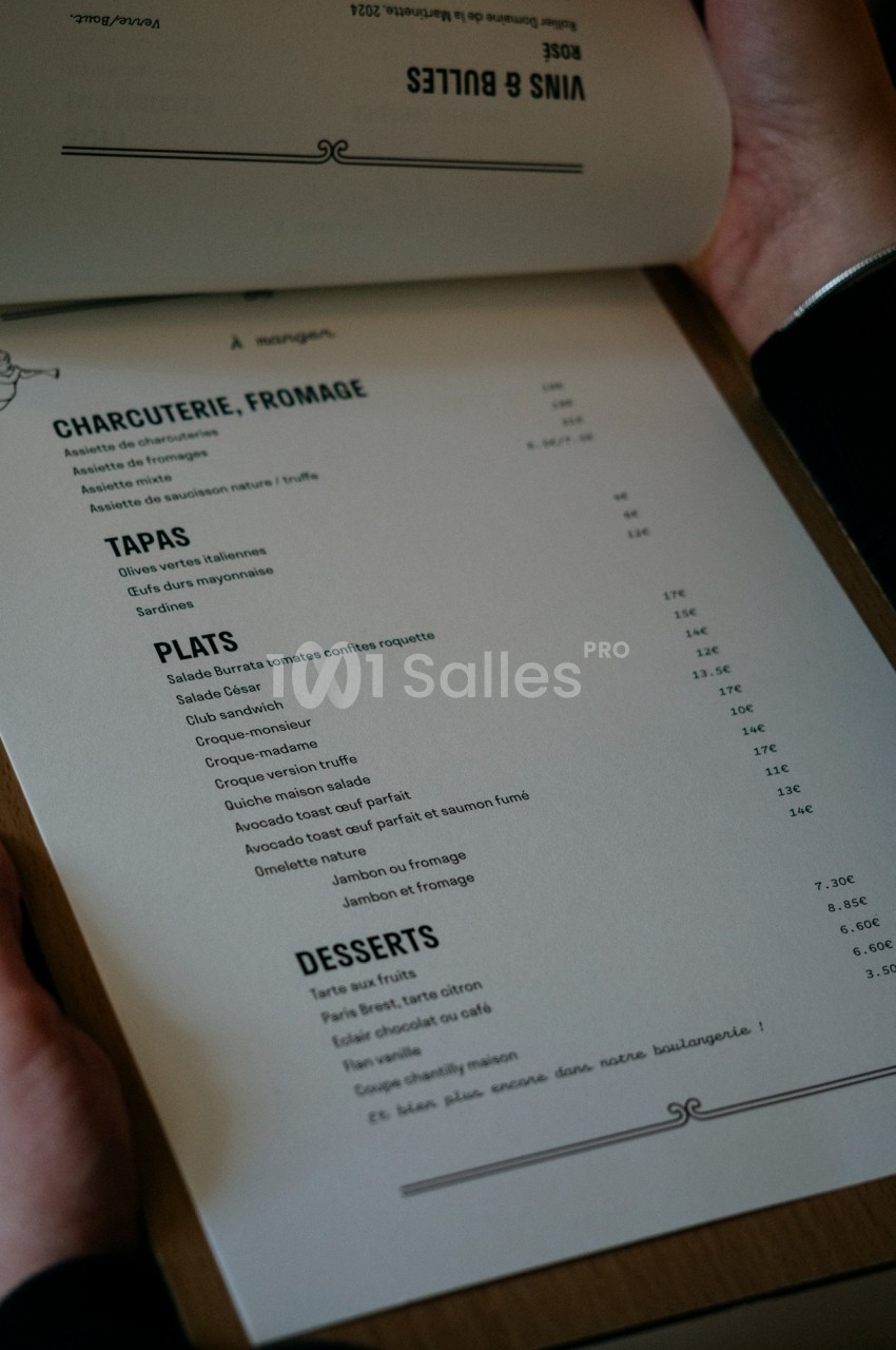 Menu imprimé tenu par une personne, listant des plats, tapas, desserts, et options de charcuterie et fromage.