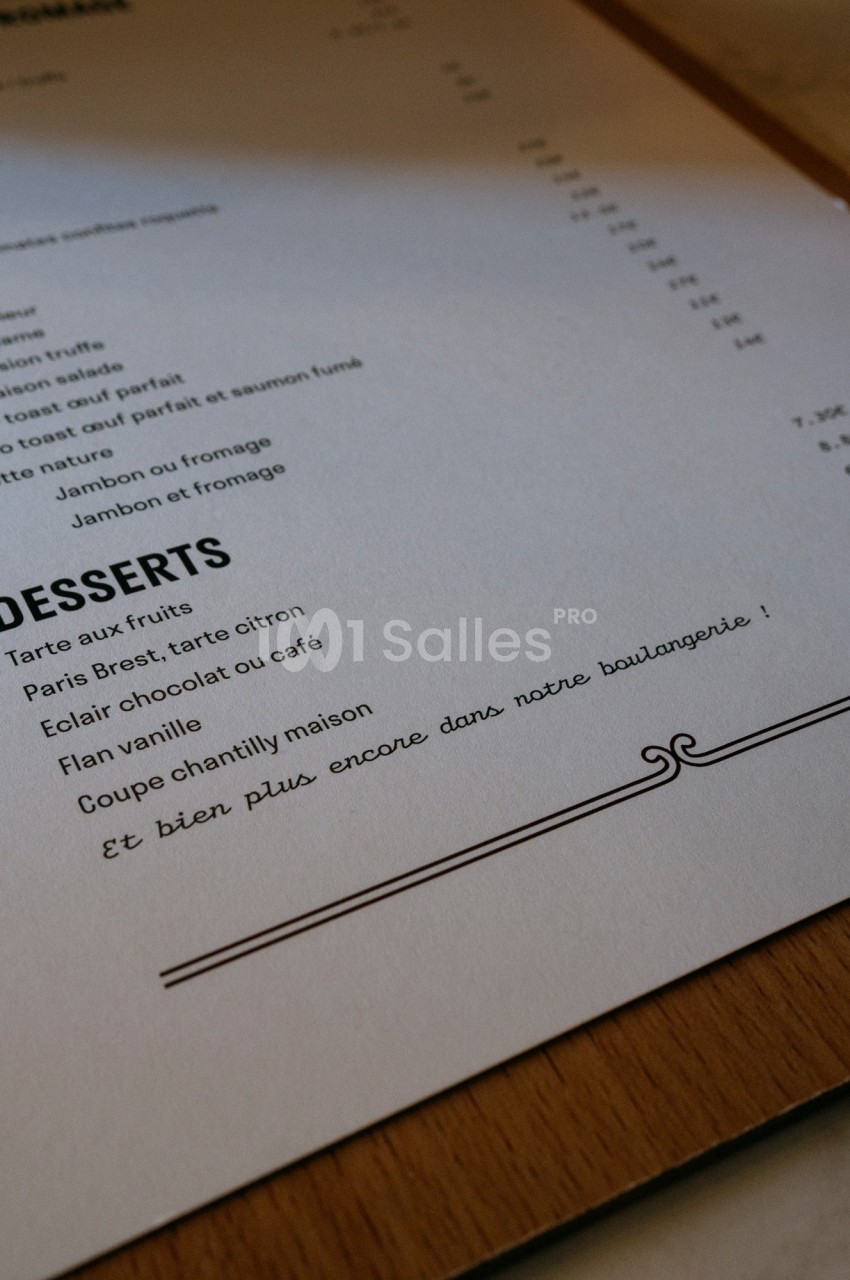 Carte de menu en papier posée sur une table, avec une section dédiée aux desserts et une note manuscrite en bas.