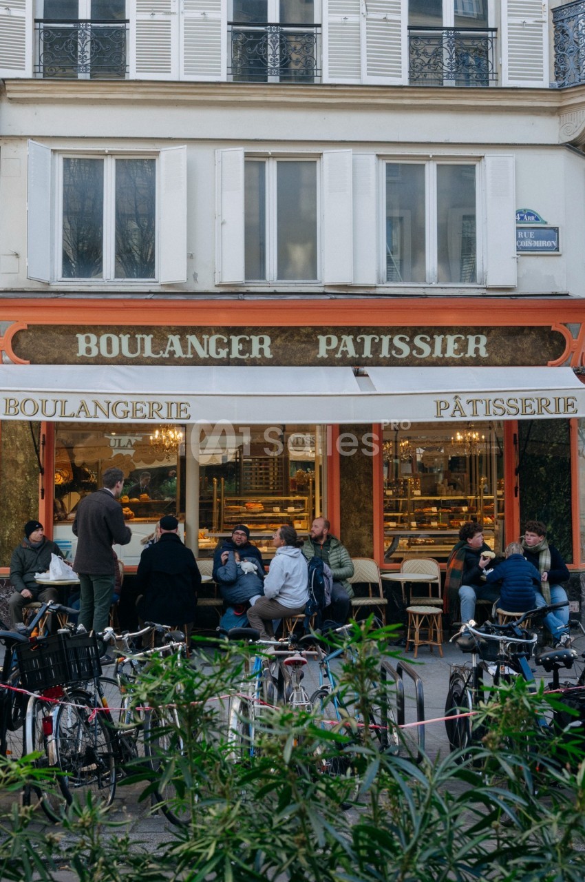 Façade d'une boulangerie-pâtisserie avec des clients assis en terrasse et des vélos stationnés devant.
