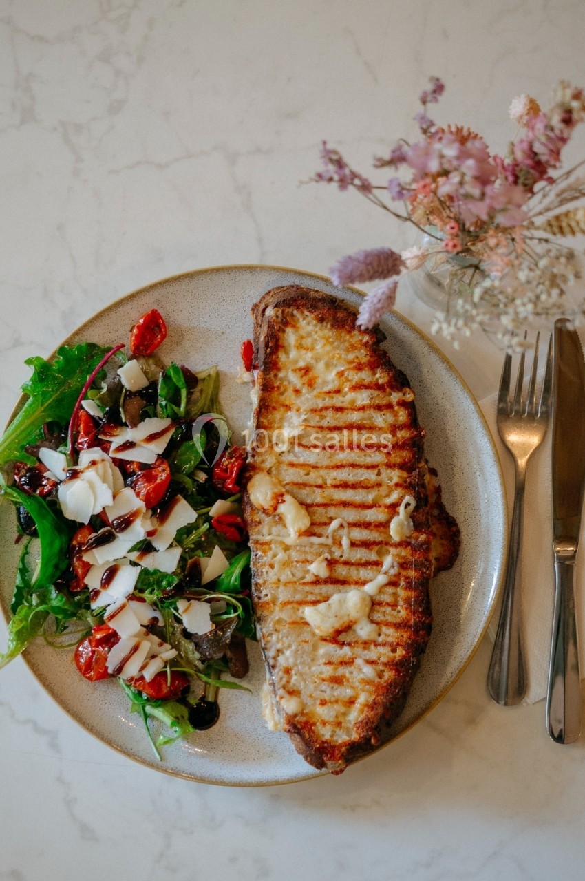 Assiette avec une tranche de pain grillé au fromage et une salade verte garnie de tomates cerises et de sauce blanche.