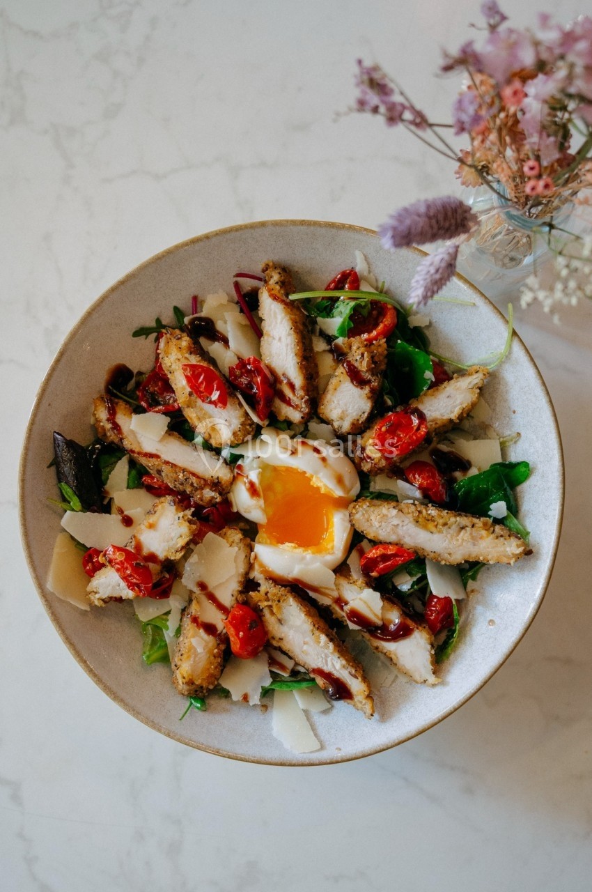 Salade composée avec morceaux de poulet grillé, tomates cerises, œuf mollet, copeaux de fromage et verdure.