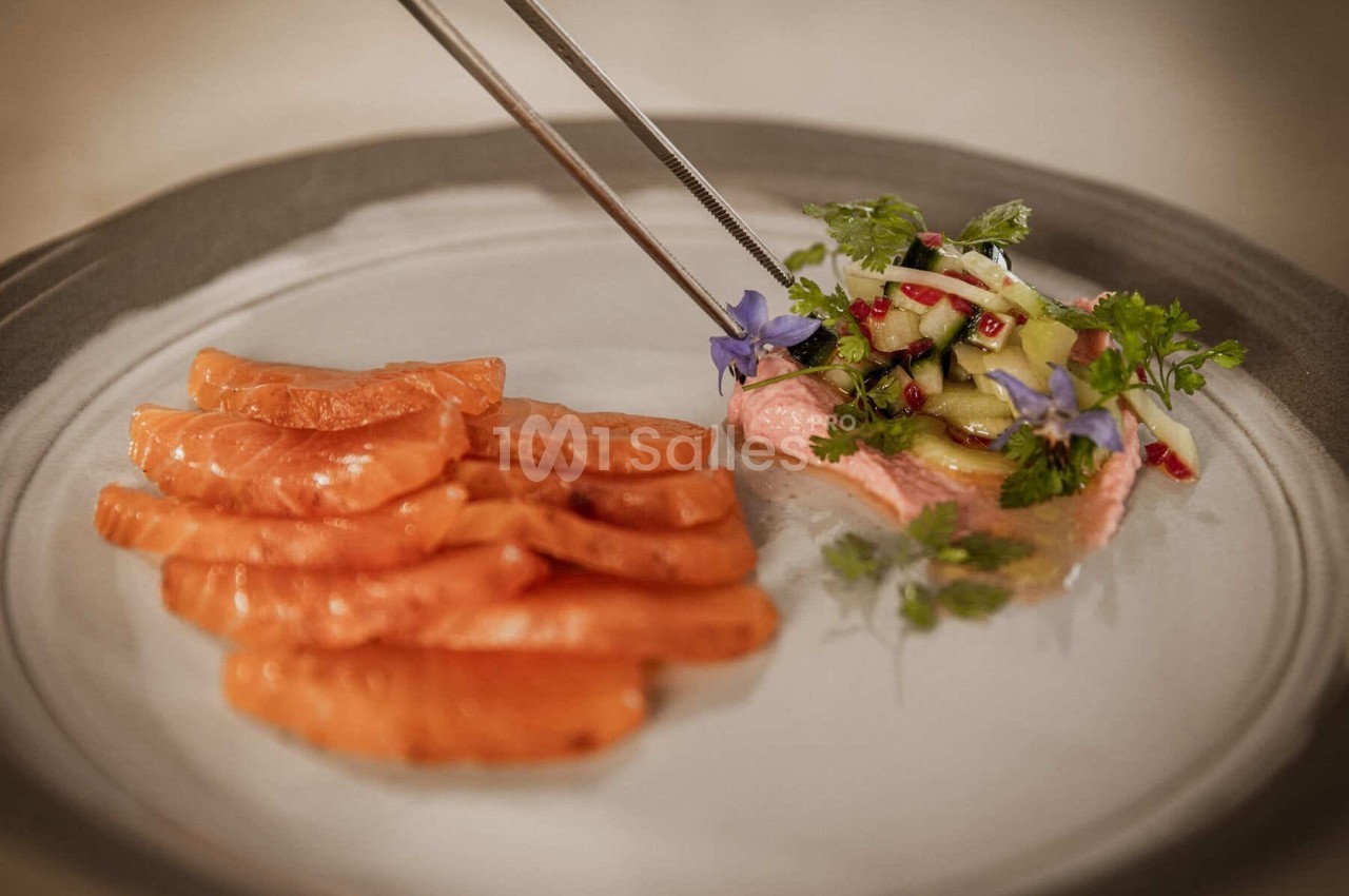 Tranches de saumon cru accompagnées d'une garniture de légumes, herbes fraîches et fleurs comestibles.