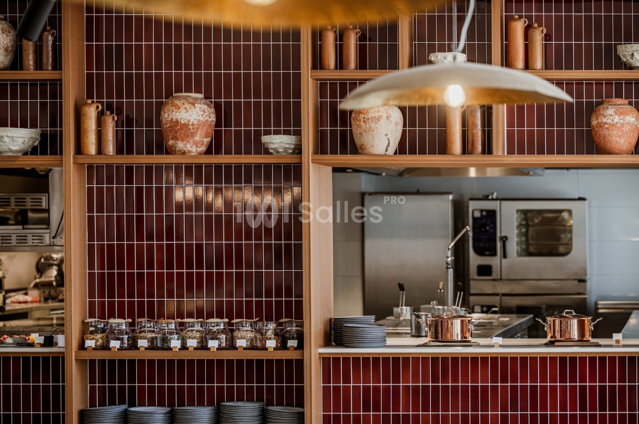 Étagères en bois avec pots en terre cuite et vaisselle, devant une cuisine ouverte avec four professionnel.
