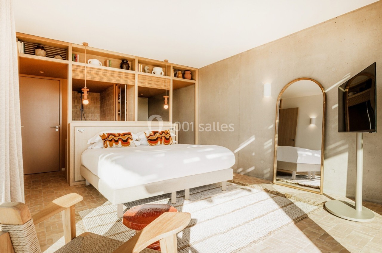 Chambre lumineuse avec lit double, miroir sur pied, étagères décorées et mur en béton apparent.