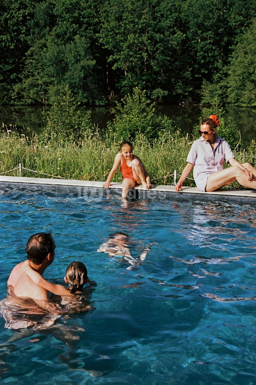 Une famille profite d'une piscine extérieure entourée de verdure par une journée ensoleillée.