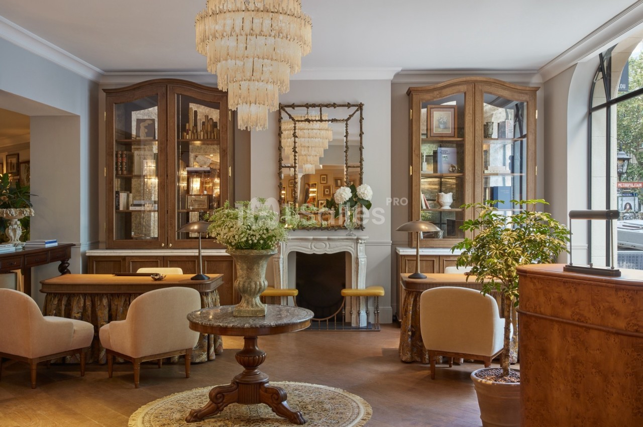 Salon élégant avec mobilier classique, lustres en cristal, cheminée ornée et grandes vitrines en bois.