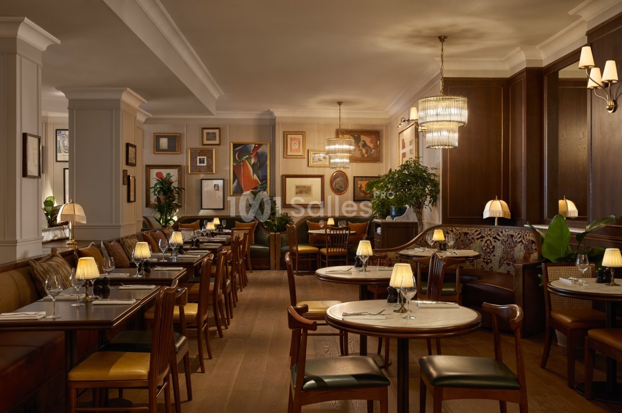 Salle de restaurant élégante avec tables en bois, chaises rembourrées, éclairage tamisé et décorations murales artistiques.