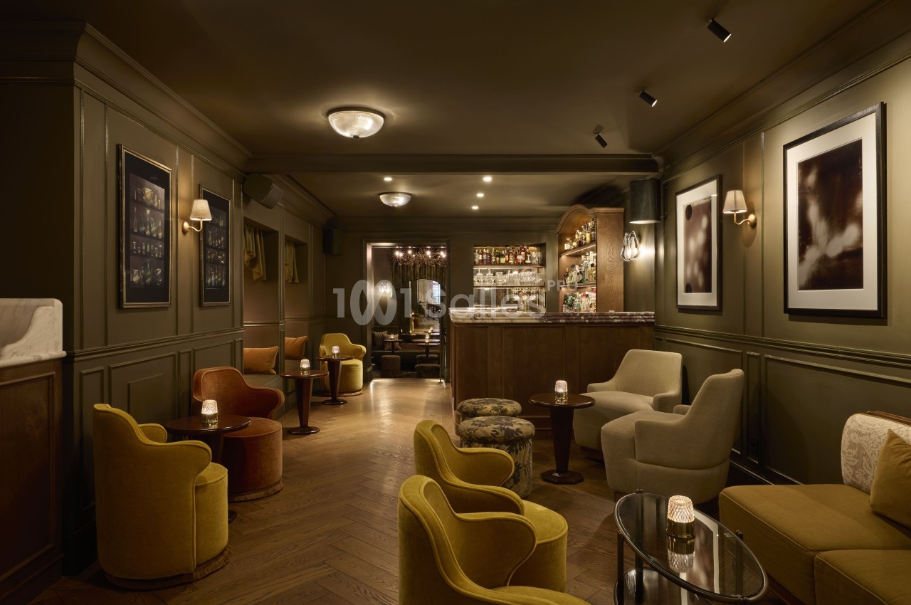 Salon élégant avec fauteuils colorés, tables basses, éclairage tamisé et bar en arrière-plan.